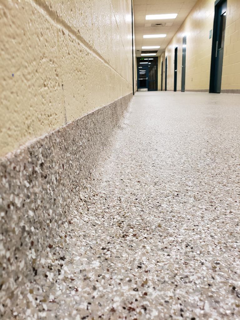 Dense fine-aggregate broadcast floor coating finished with an integral cove base